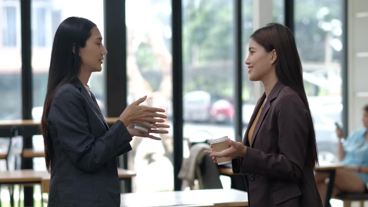 两个穿西装的女人在咖啡馆里聊天。其中一个拿着杯子。另一个女人拿着一个钱包视频下载