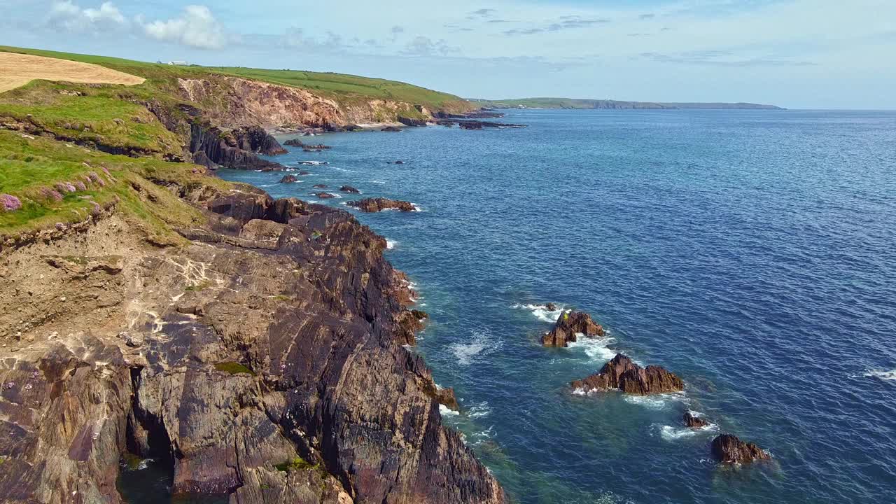 海岸线是多岩石的，后面是长满草的山坡。大海平静，天空万里无云。视频素材