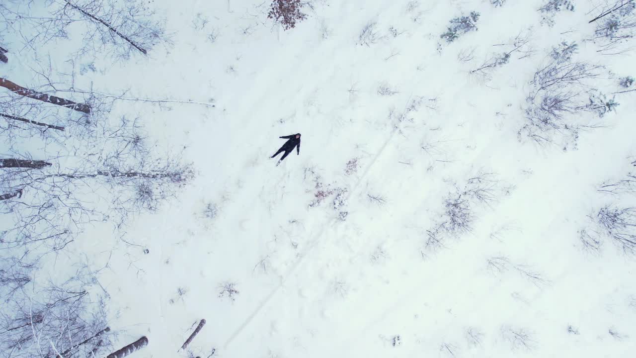 男子躺下造雪天使，俯视图鸟瞰美丽的白雪皑皑的冬季森林。冬天雪地里的路。霜晨旅行概念背景。令人惊叹的冬季景象。圣诞节的主题。云杉覆盖视频下载