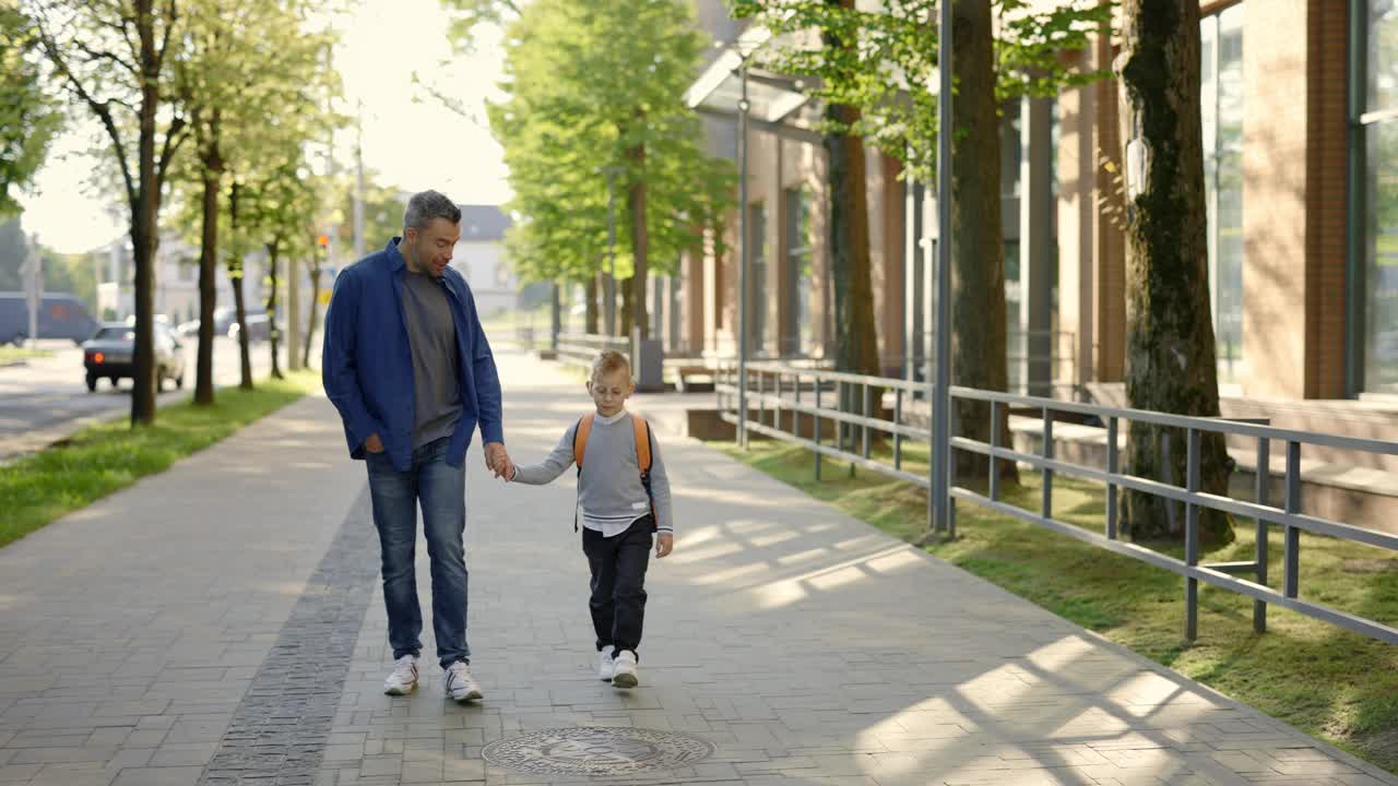 回到学校。小孩子拿着包，手牵着他的父亲。送儿子上学的男性。教育和家庭的概念。视频素材