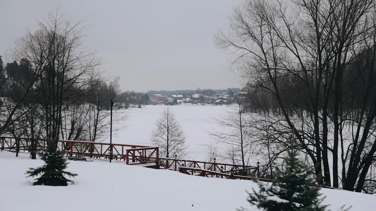 冬天，在树枝后面的河堤上，可以看到一条被雪覆盖的冰冻河流。拍摄美丽的冬日大自然视频下载