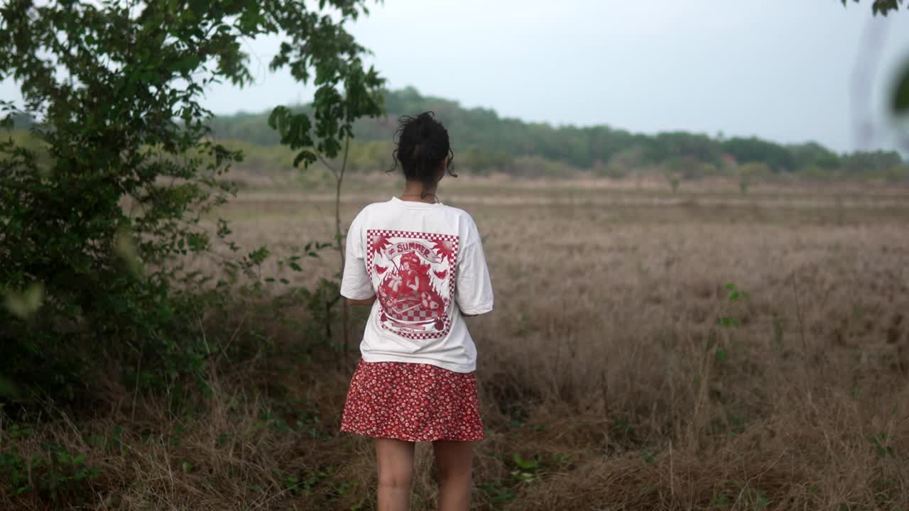 穿着白衬衫和红裙子的年轻女子走过一片干燥的草地视频素材