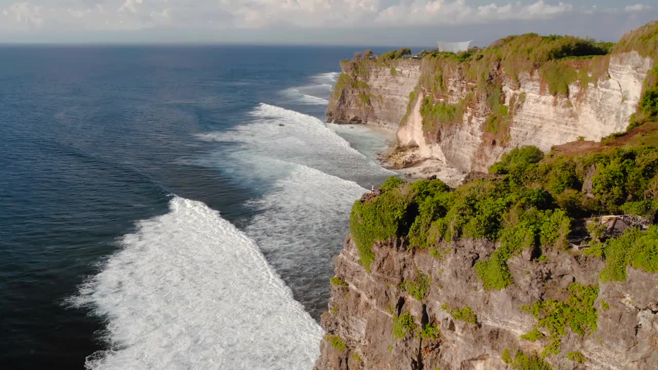 印尼巴厘岛乌鲁瓦图，一个人站在海滩和海洋旁边的悬崖上视频素材