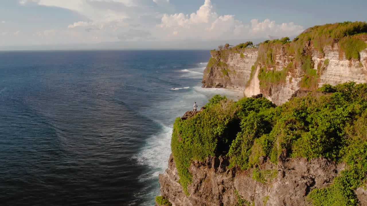 印尼巴厘岛乌鲁瓦图，一个人站在海滩和海洋旁边的悬崖上视频素材