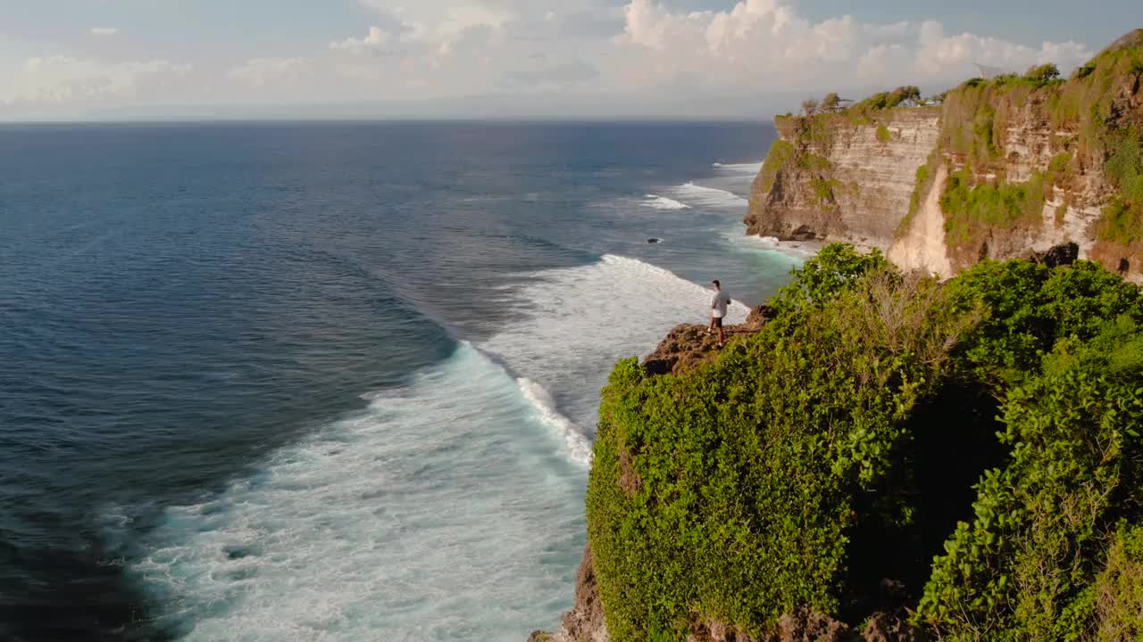 印尼巴厘岛乌鲁瓦图，一个人站在海滩和海洋旁边的悬崖上视频素材