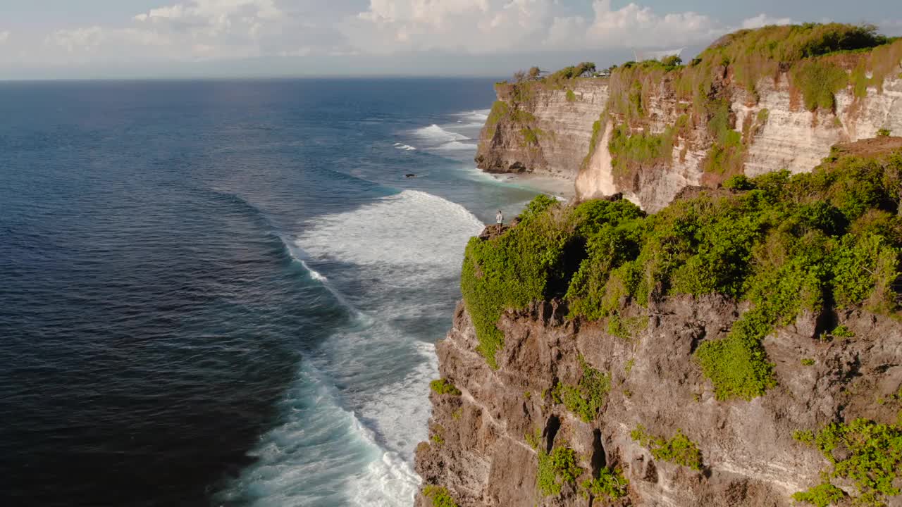 印尼巴厘岛乌鲁瓦图，一个人站在海滩和海洋旁边的悬崖上视频素材