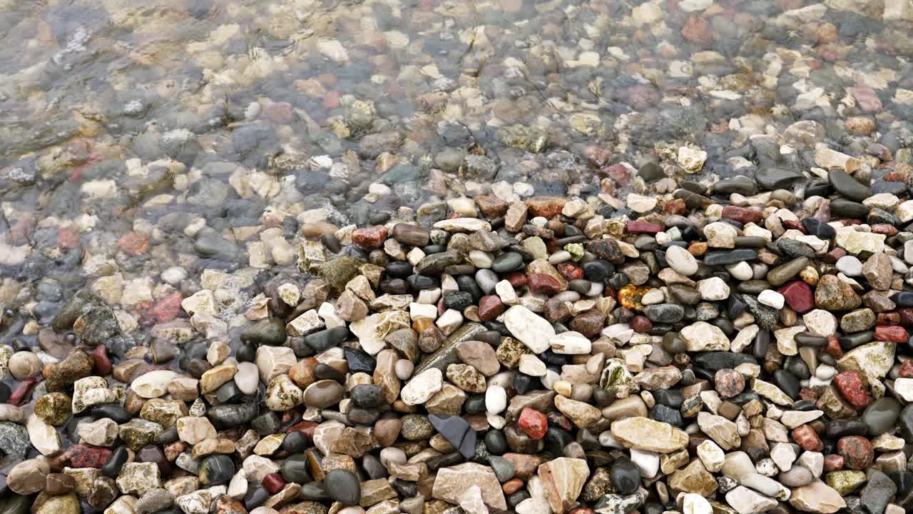 平静的海浪轻轻地拍打着日出时海边的彩色石头视频下载