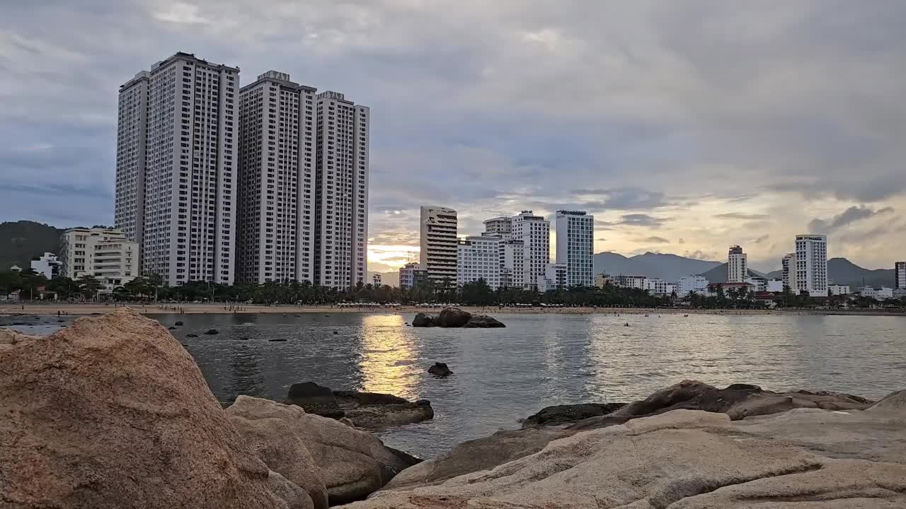 日落中的越南芽庄市的海滩、山、岩石和高层建筑。视频素材