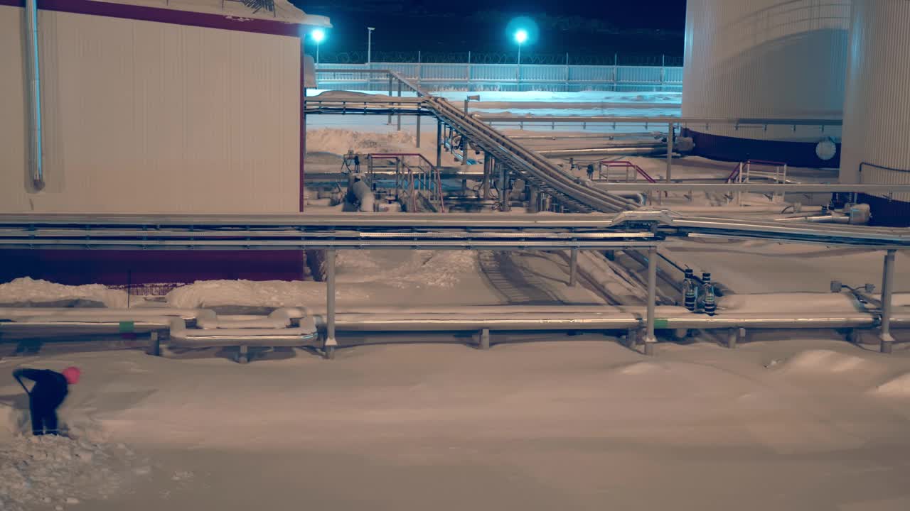 在工业灯光的照耀下，工人们在夜间清理工厂的积雪，尽管冬季条件恶劣，但他们仍在努力保持生产和安全标准。时间流逝视频素材