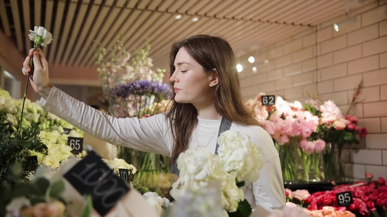 在花店的冰箱里，女花师正在整理鲜花。在花店里，年轻的女售货员正在准备订货。手里拿着花的女人视频下载