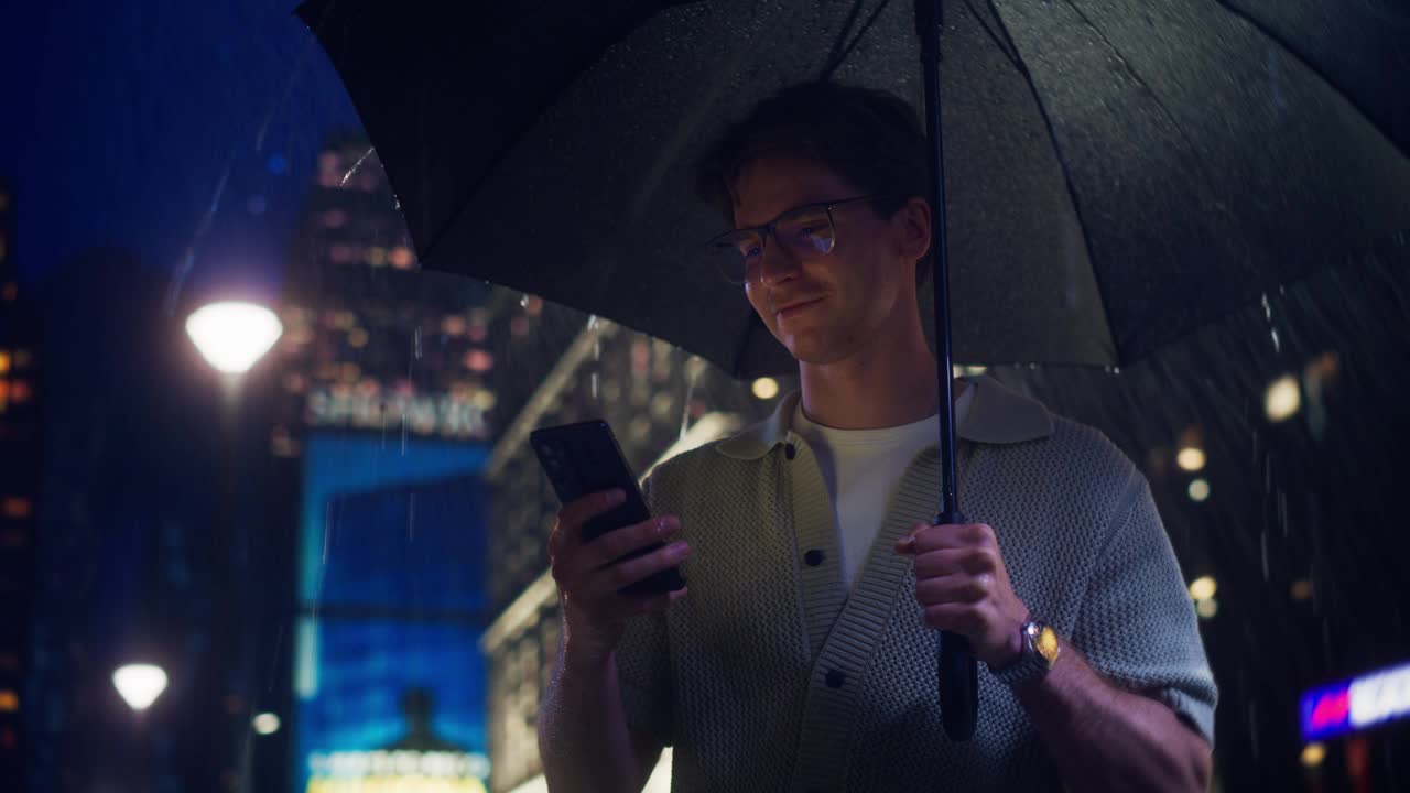 白人男子用智能手机，站在红色雨伞下避雨。年轻男性使用互联网，查看社交网络动态，阅读新闻更新，在线与朋友保持联系视频素材