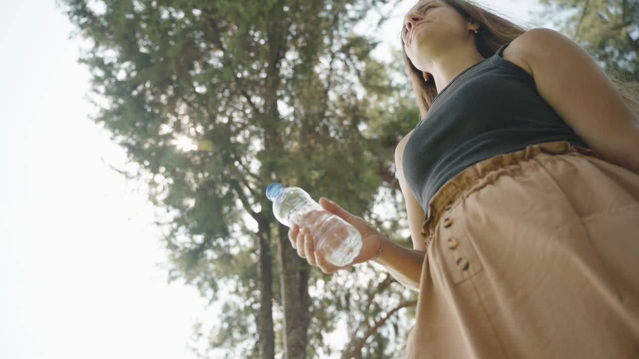 喝水，一位年轻女子在树下保持水分。宁静的环境增添了这一刻。视频素材