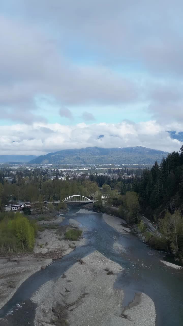 风景河流在桥下流动的垂直视频。城市、树木和山脉。弗雷泽山谷，不列颠哥伦比亚省，加拿大。视频素材