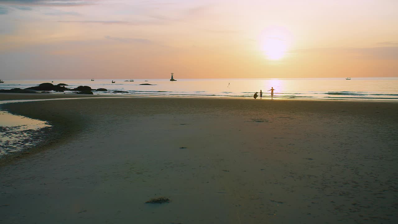 一个宁静的海滩景观，宁静的日落在海上与家人享受时刻海浪在背景，他们的剪影在金色的天空，传达自由与和平的感觉视频素材