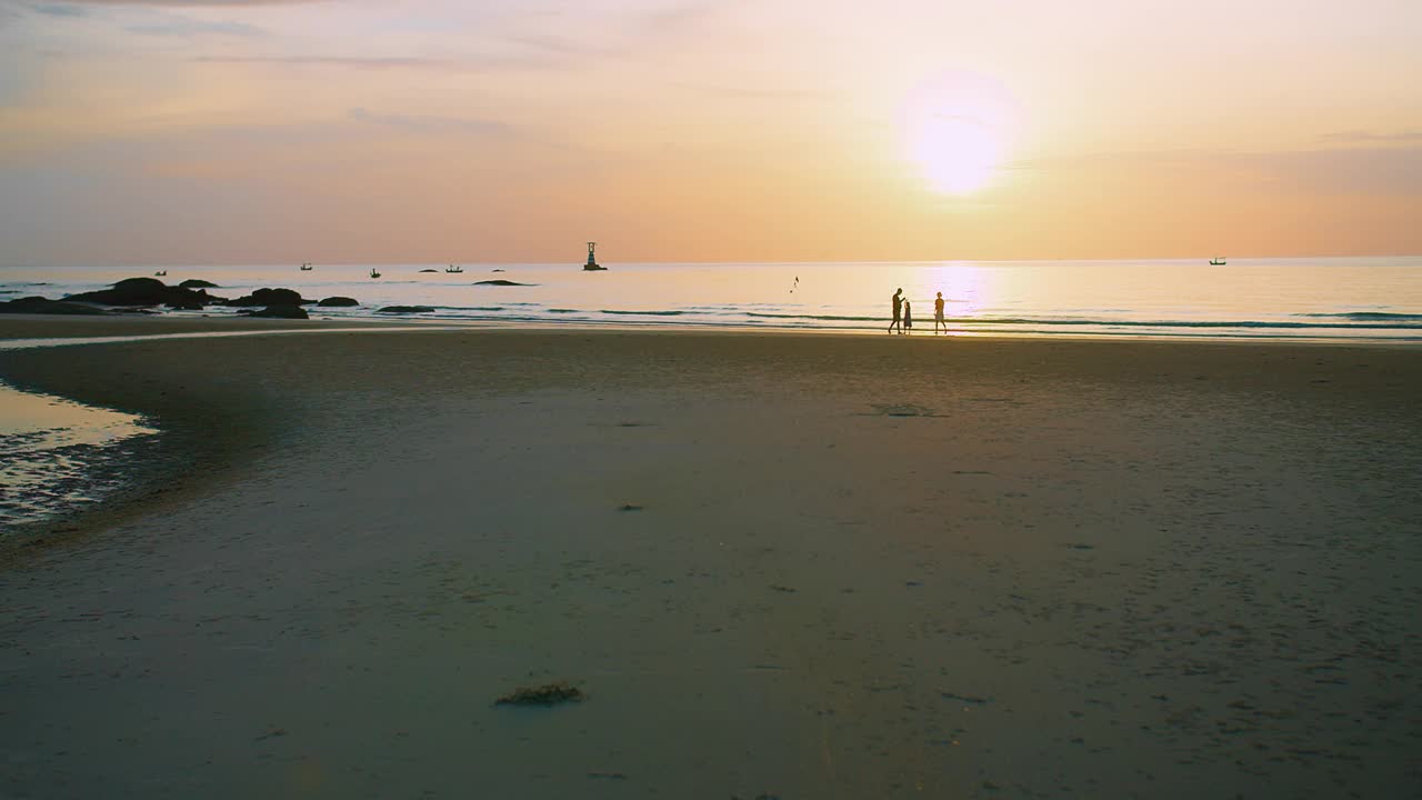 一个宁静的海滩景观，宁静的日落在海上与家人享受时刻海浪在背景，他们的剪影在金色的天空，传达自由与和平的感觉视频素材