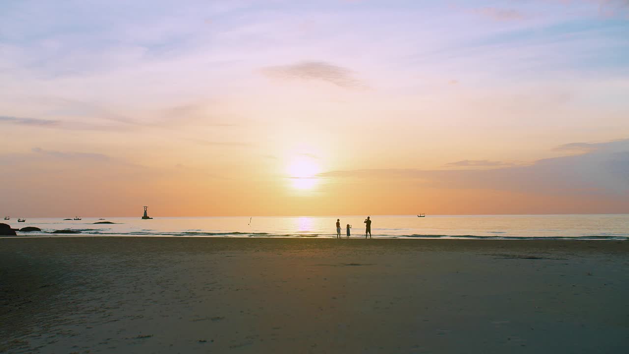 一个宁静的海滩景观，宁静的日落在海上与家人享受时刻海浪在背景，他们的剪影在金色的天空，传达自由与和平的感觉视频素材