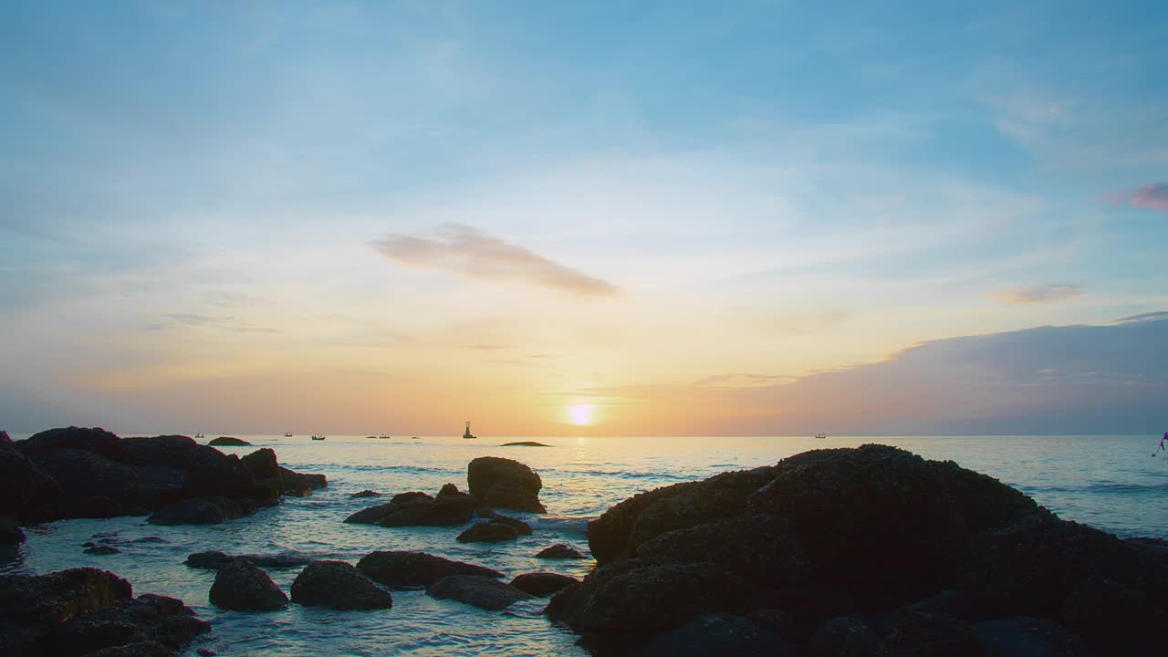 日落时宁静的海岸景色，有岩石海岸线，平静的海浪，远处的灯塔在五彩缤纷的天空下。视频素材