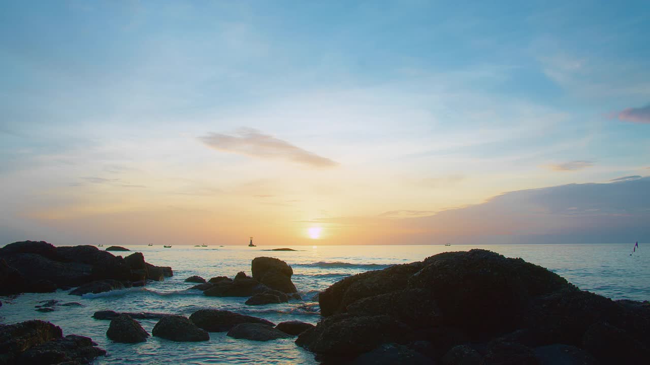 日落时宁静的海岸景色，有岩石海岸线，平静的海浪，远处的灯塔在五彩缤纷的天空下。视频素材