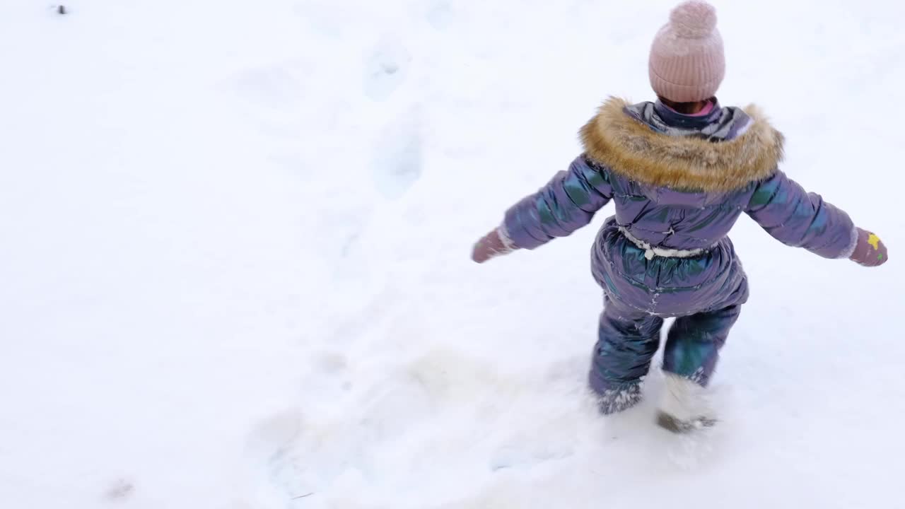 一个穿着蓝色连体衣的女孩在雪地里制作雪天使。冬季乐趣，户外游戏，圣诞节视频下载