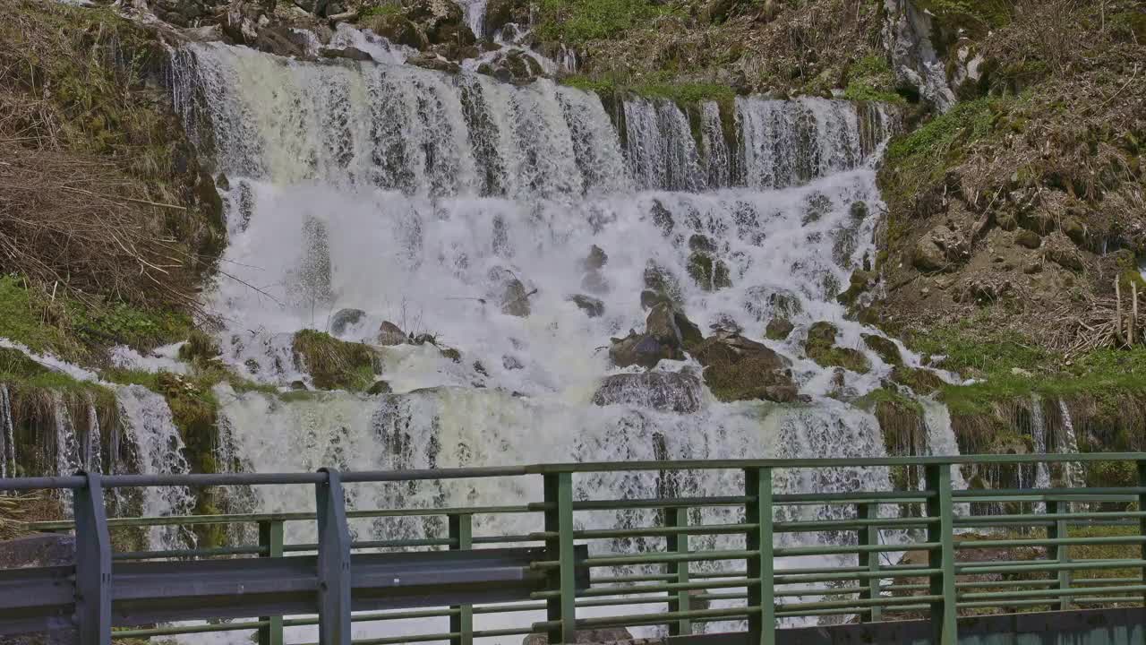 瀑布在山间，桥的旁边。水从瀑布倾泻而下。格拉鲁斯州内菲尔斯附近的Rauti瀑布视频下载