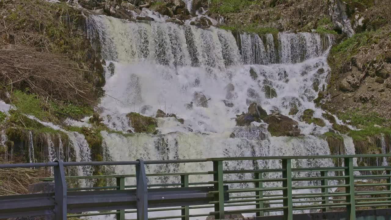 瀑布在山间，桥的旁边。水从瀑布倾泻而下。格拉鲁斯州内菲尔斯附近的Rauti瀑布视频下载