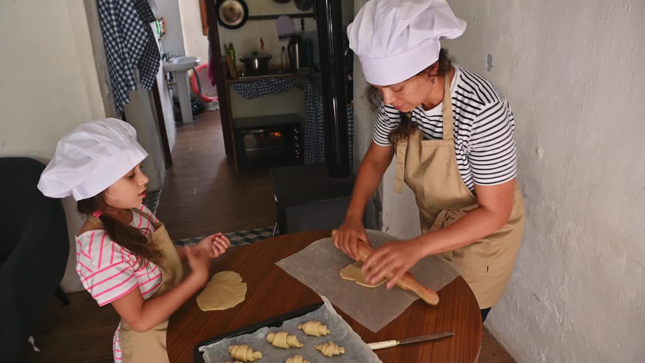 母女俩戴着厨师帽，围着围裙，在舒适的厨房里一起烤饼干视频素材