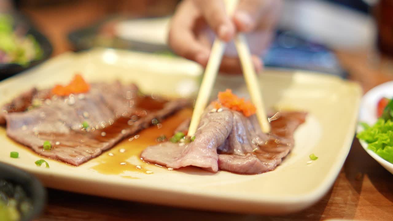 (特写)在日本餐厅用筷子夹起桌上的热烤肉。视频素材