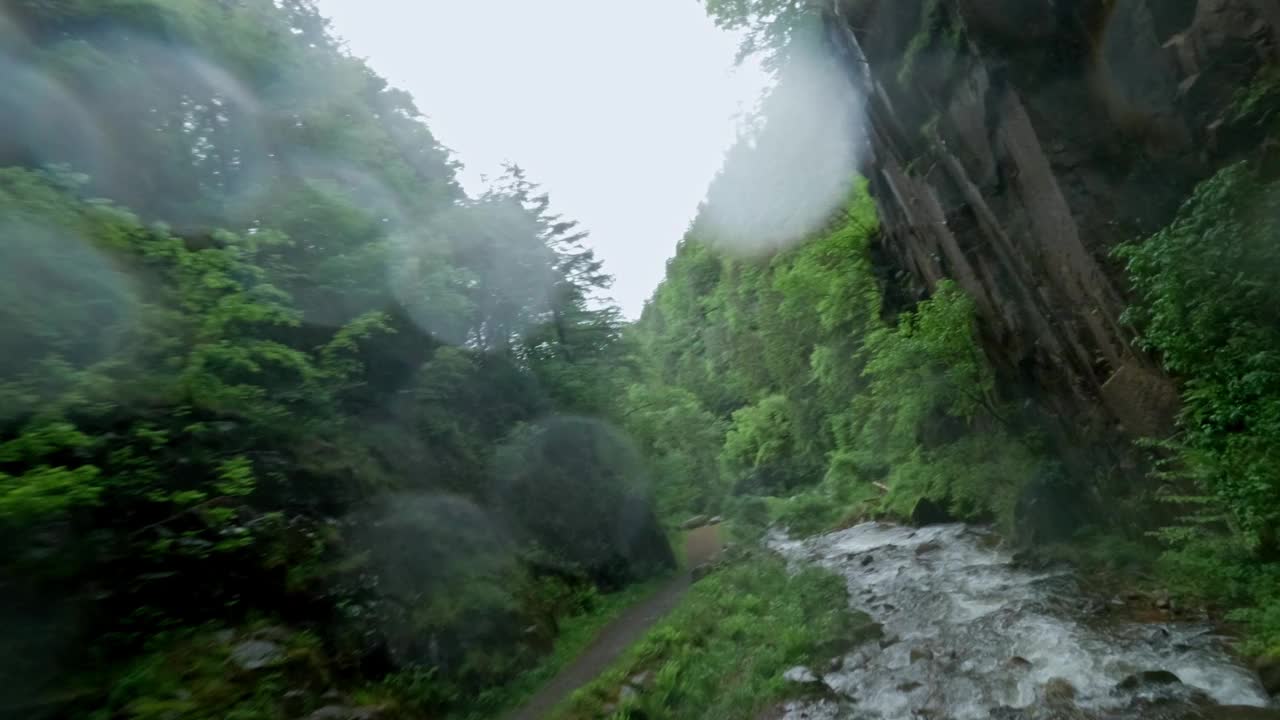 郁郁葱葱的绿色峡谷，瀑布倾泻而下，雾蒙蒙的气氛在下雨天拍摄视频素材