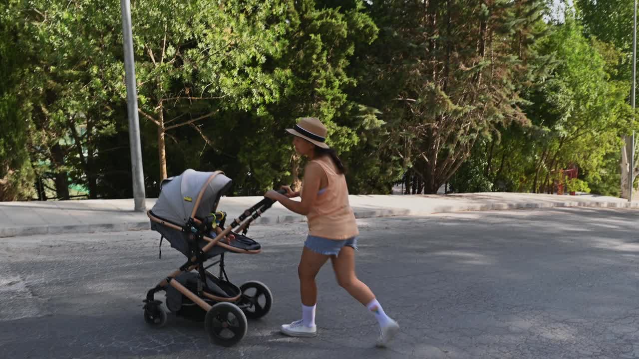 在一个阳光明媚的日子里，一个年轻女子在公园里推着婴儿车视频素材