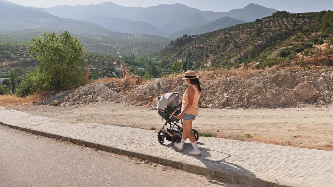 在一个阳光明媚的日子里，一名妇女推着婴儿车在风景秀丽的山区散步视频素材