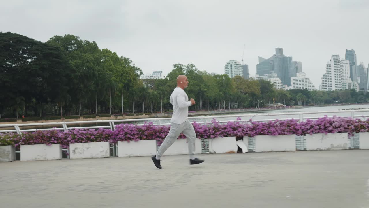 穿着运动服的运动男子沿着城市堤岸晨跑。慢跑从最初的光开始，唤醒身体和心灵。慢跑时，男人呼吸着新鲜的城市空气，让自己一整天都充满活力。视频下载