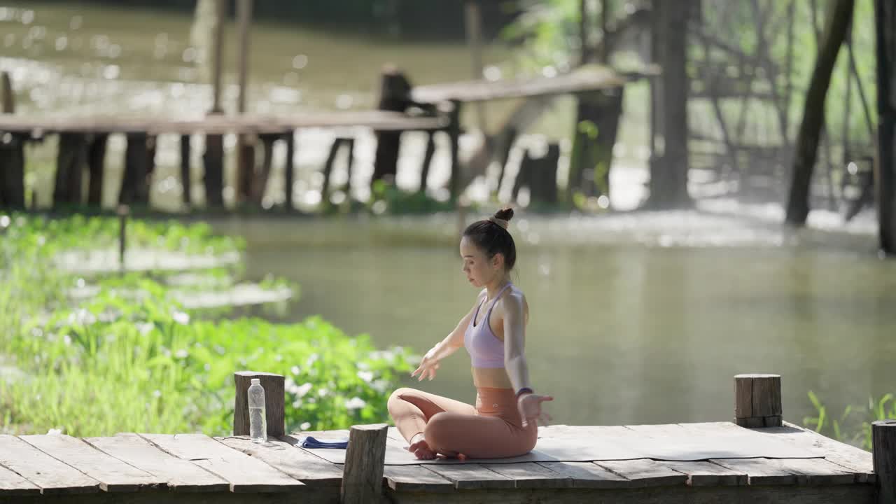 一个女人坐在水边的码头上练习瑜伽视频素材