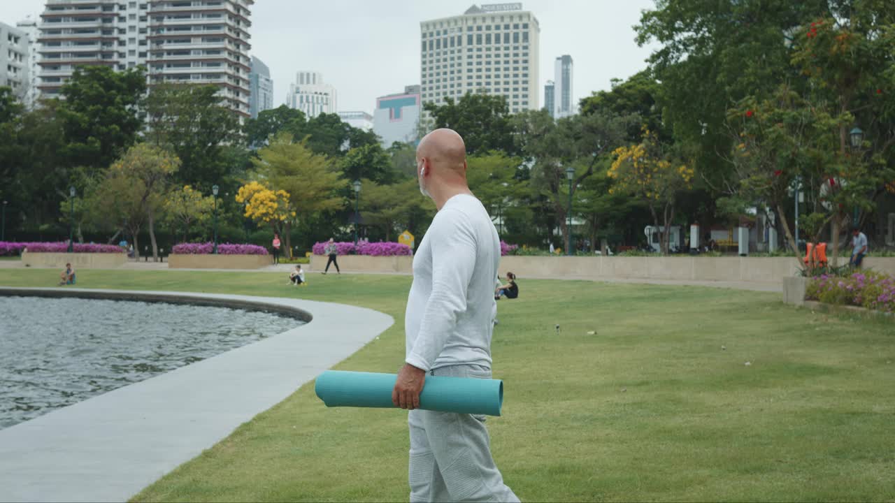 教练穿着运动服，手拿垫子，在公园里欣赏池塘的美景。宁静的公园氛围是户外活动的理想选择。教练在公园里准备上课，探索周围的美景。视频素材