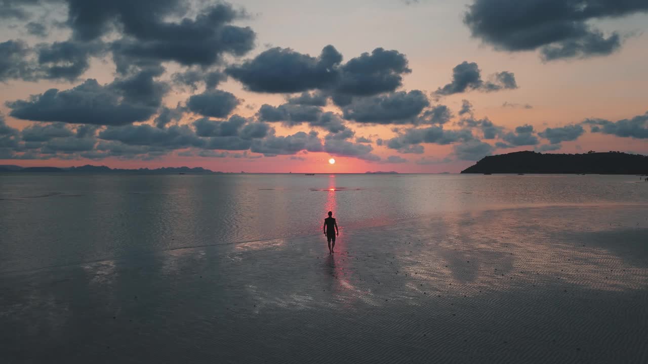 在日落剪影的人走在沙滩上橙色的夕阳美景。宁静的海边和日落的气氛，鲜艳的天空，纯净的宁静，欣赏大自然的奇观日落。视频素材