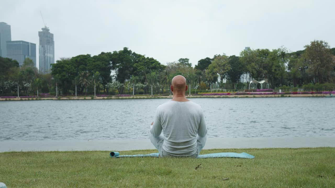 成熟的男人在做安静的冥想坐着城市公园的背影正念的呼吸通过冥想释放紧张的压力。城市公园的人正在冥想练习，连接自己和自然世界。视频素材