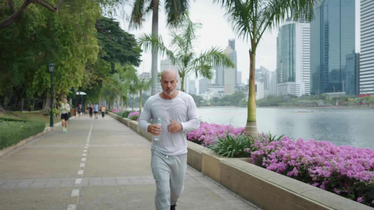 绿色植物城市公园成熟的运动员慢跑者跑步慢跑者体现了决心，专注，坚定不移，突破他的极限。暂停片刻，喘口气，慢跑者追求他的健身目标。视频素材