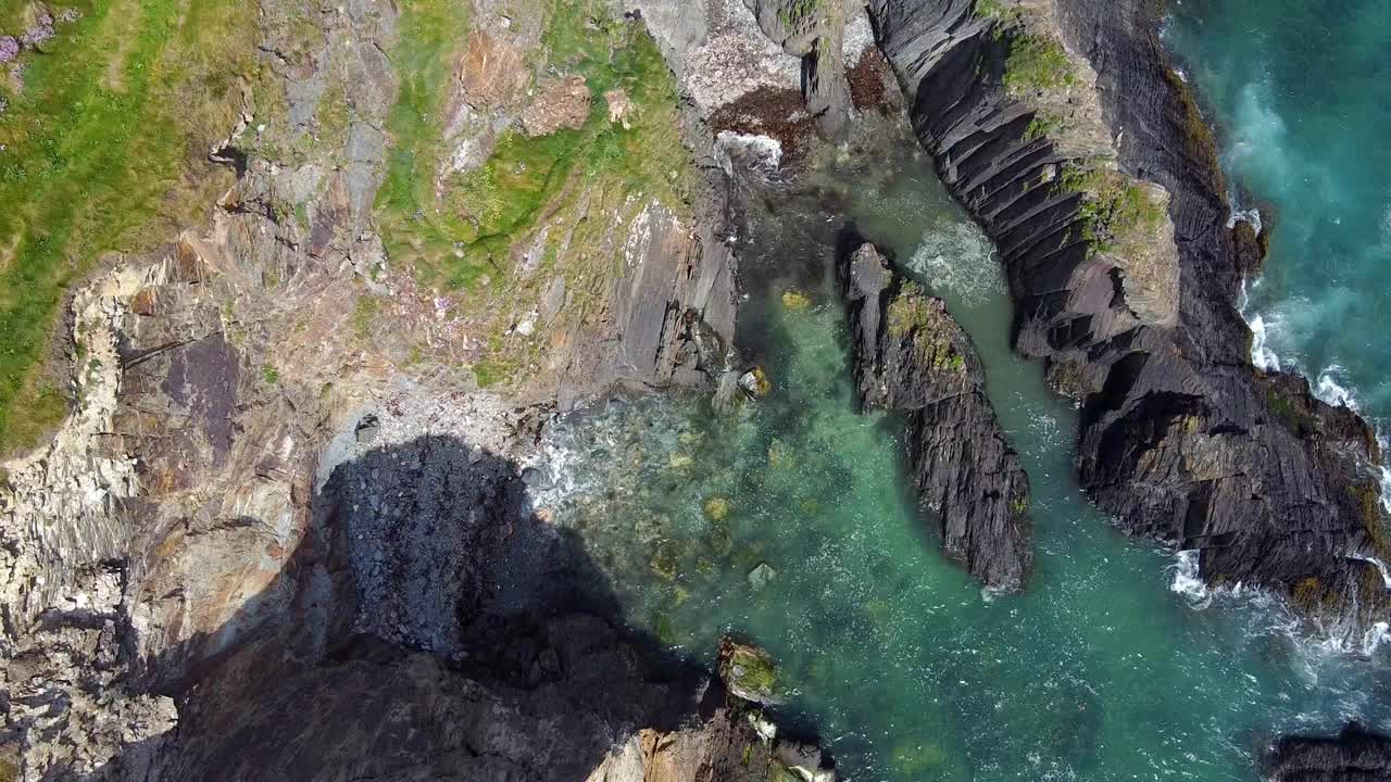 鸟瞰蓝绿色海水的岩石海岸线。岩石呈深灰色，有纹理。在水面上可以看到白浪。视频素材