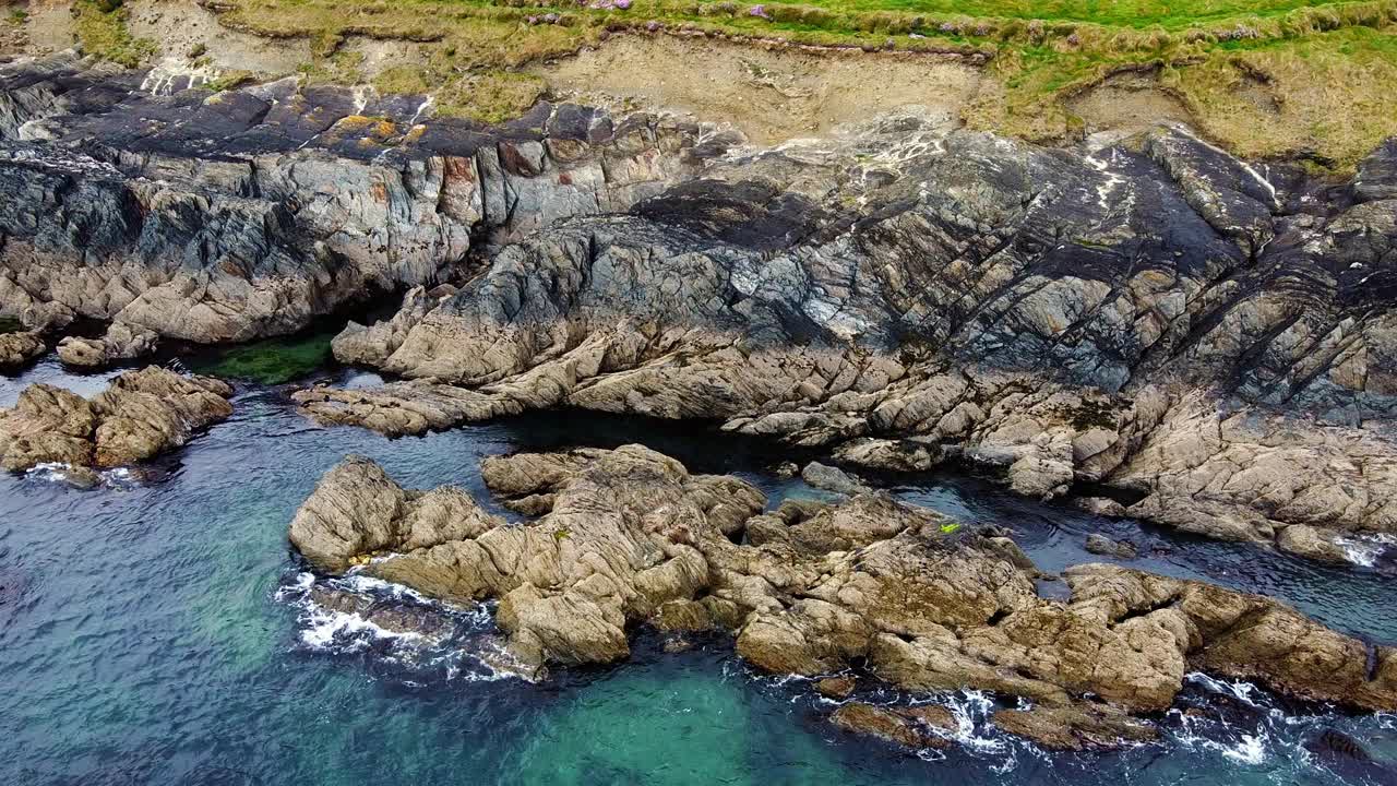 海浪冲击着岩石海岸线，形成水花，留下一串泡沫。视频素材