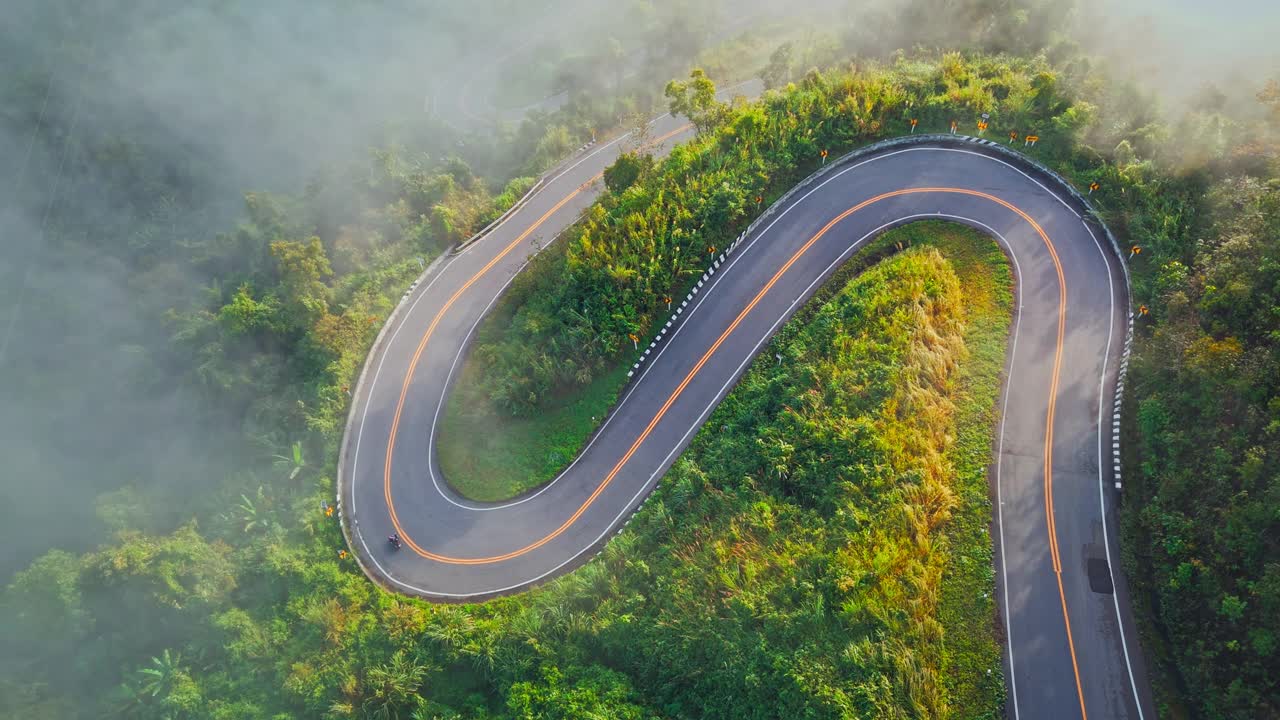 清晨森林中的乡村公路鸟瞰图。无人驾驶飞机飞过乡村公路，在山间有雾。泰国南省的标志性旅游景点视频下载