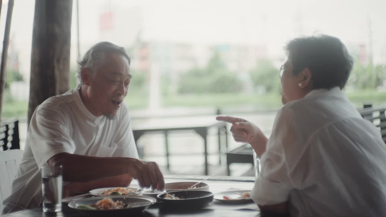 快乐的亚洲老人坐在外面的餐厅吃饭。视频素材