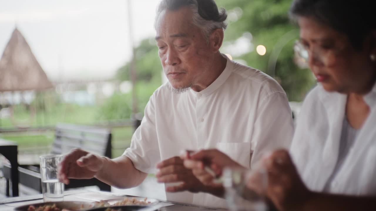 快乐的亚洲老人坐在外面的餐厅吃饭。视频素材