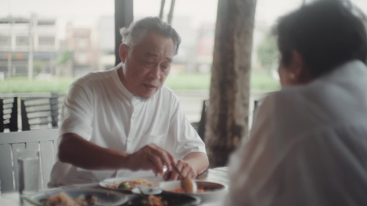 快乐的亚洲老人坐在外面的餐厅吃饭。视频下载