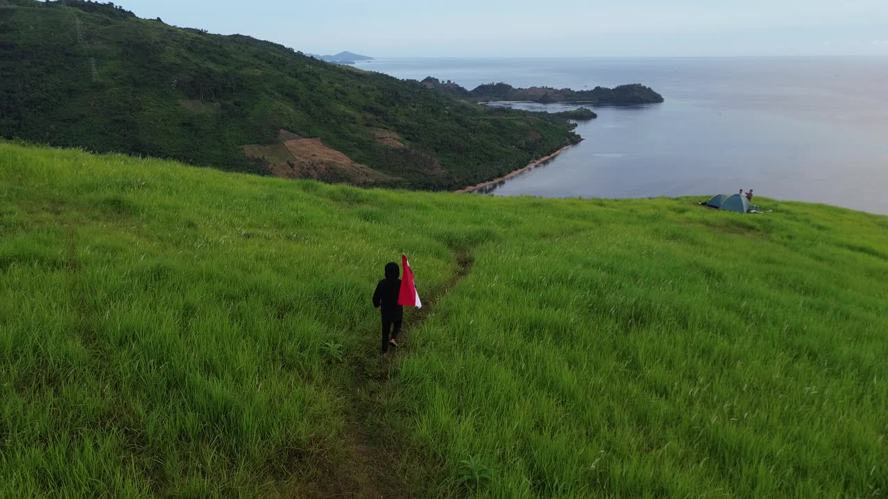 鸟瞰图:一名男子在印尼哥伦塔洛的杜努山顶挥舞着印尼国旗视频下载