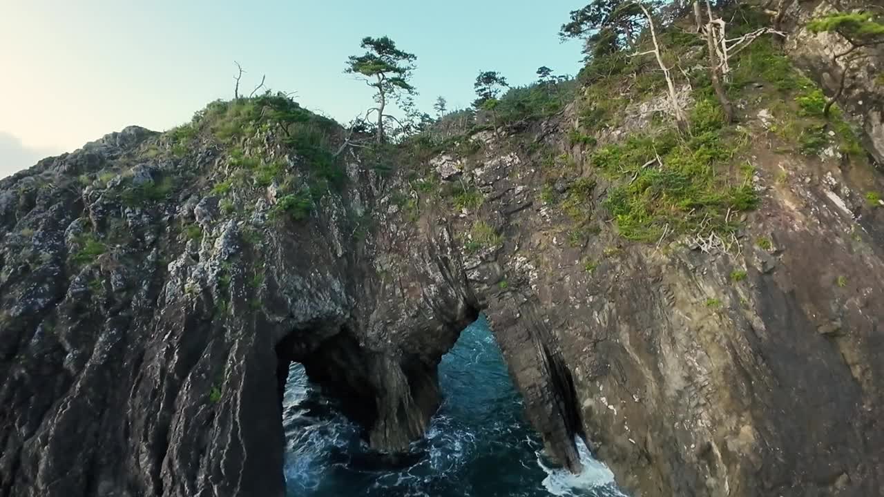 FPV在岩石海岸线上的悬崖上飞过树缝视频素材