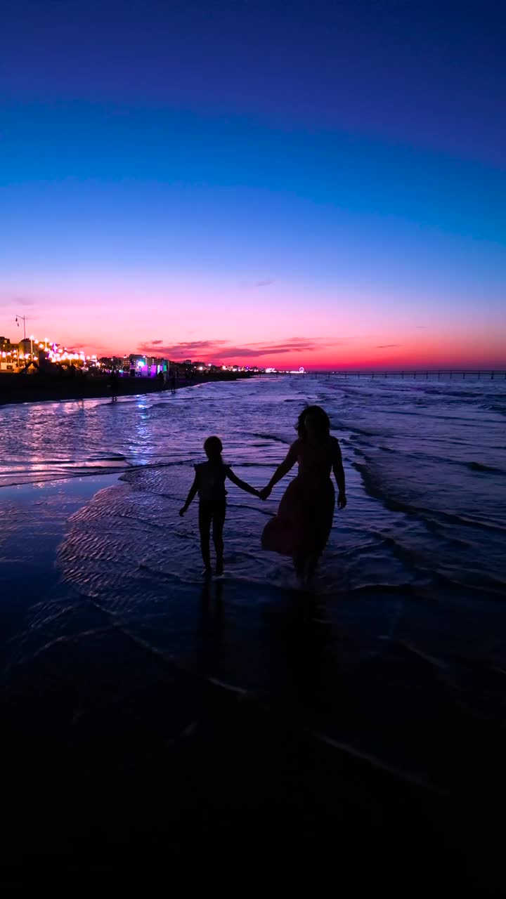 在美丽的夕阳下，母亲和女儿在海滩上散步的剪影。里米尼,意大利视频下载