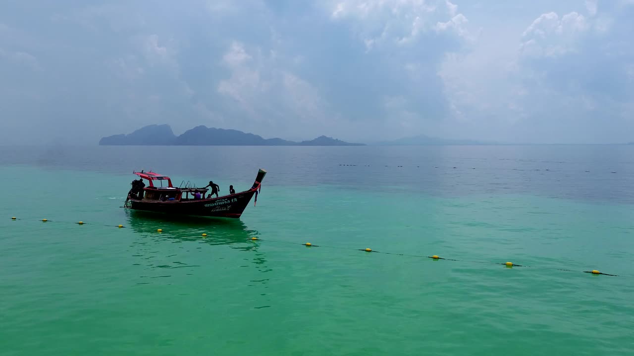 鸟瞰图的长尾船航行在清澈的海洋与可见的珊瑚礁与背景的Koh Kradan岛的观点。Koh kradan，庄，泰国视频下载