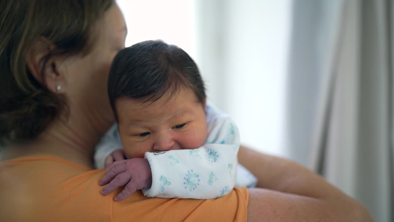 奶奶轻轻地把刚出生的孙子抱在肩上，给他安全感和安慰。宝宝平静的举止凸显了他们之间的关爱和纽带视频素材