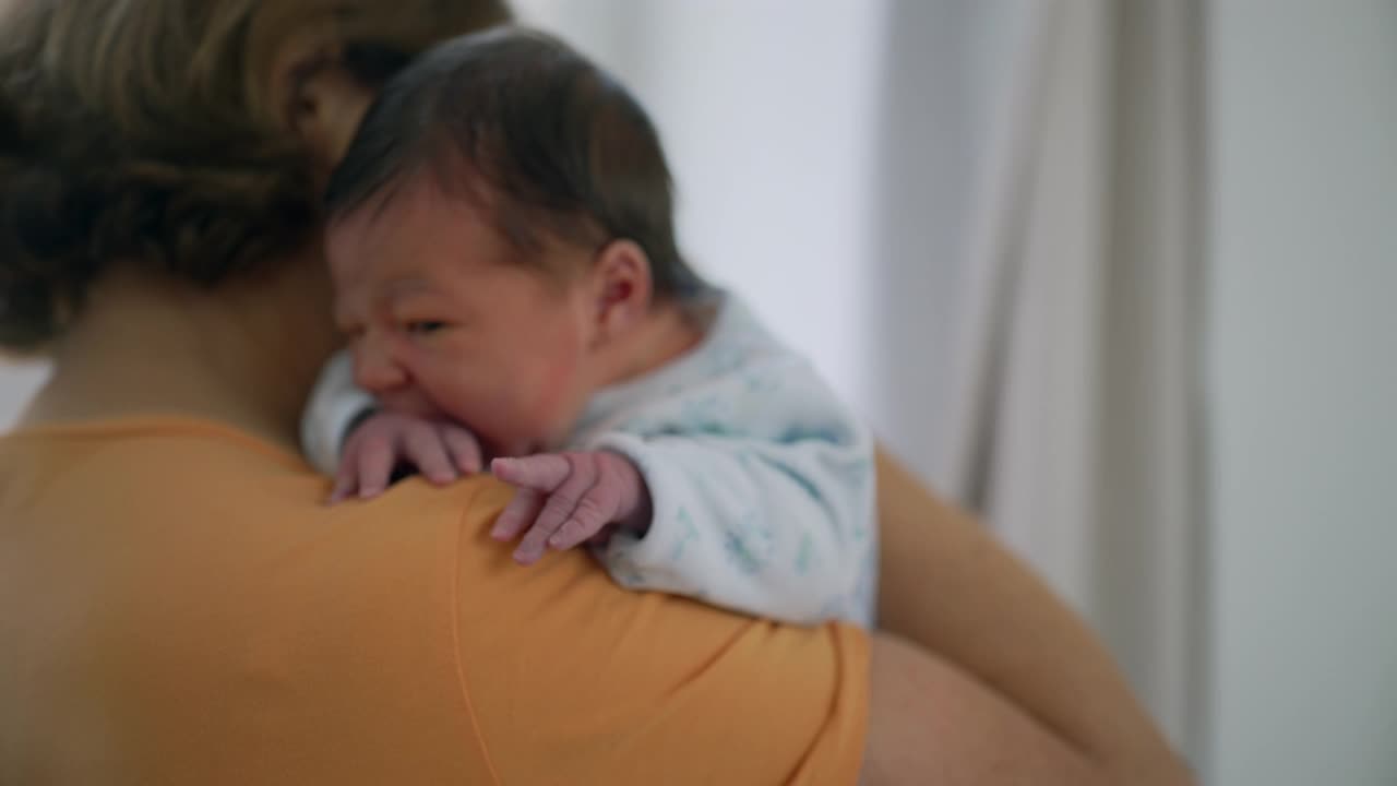 奶奶在肩上安抚刚出生的孙子，孩子的小手轻轻地抓着她的衬衫。温暖，舒适，以及两代人之间的特殊联系视频素材