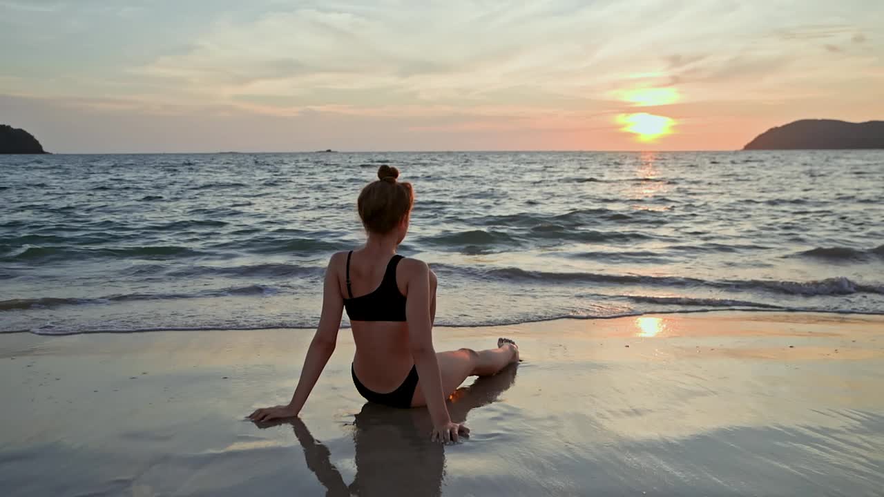 女子坐在海边的后视图，在海滩上欣赏日落视频下载