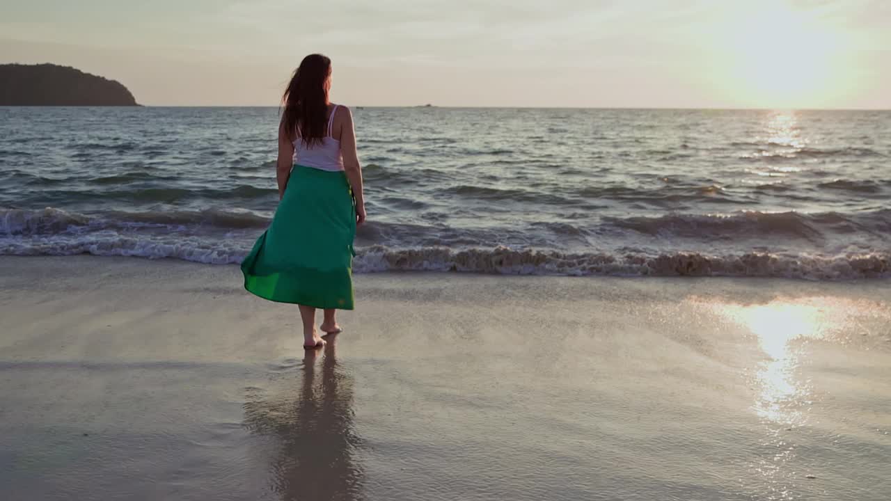 夕阳下，女子在沙滩上走向海景的后视图视频素材